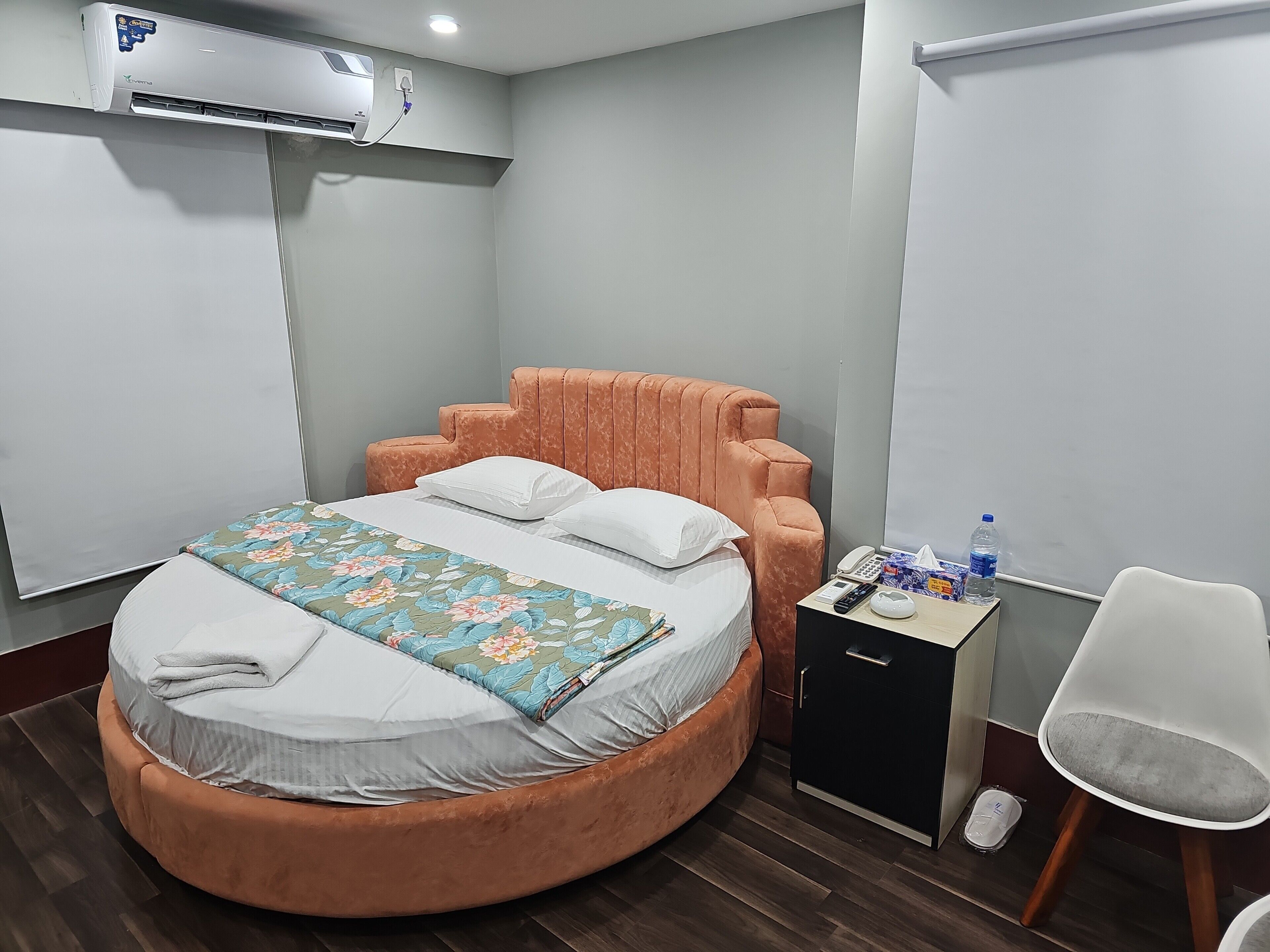 Un dormitorio con una cama redonda, un escritorio pequeño con un teléfono y artículos de aseo, y un equipo de aire acondicionado.