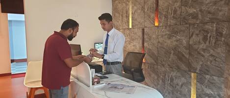 A reception desk with a marble countertop, a computer, and a newspaper. There is a chair and a wall with vertical light strips.