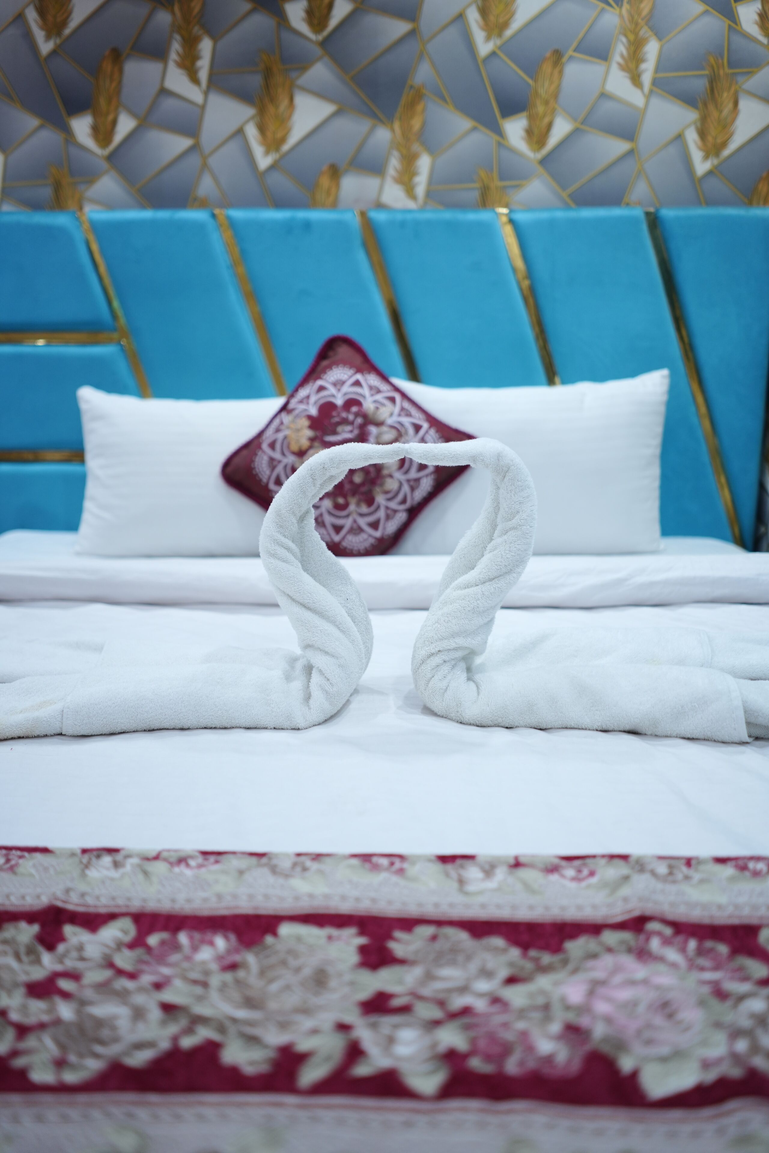 A bed with white linens, a decorative pillow, and two towels arranged in a swan shape.