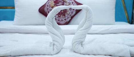 Una cama con sábanas blancas, una almohada decorativa y dos toallas dispuestas en forma de cisne.