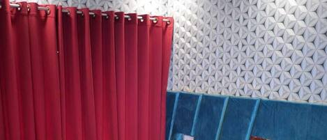 A hotel room with a bed, red curtains, a white pillow, a white towel, and a blue headboard.