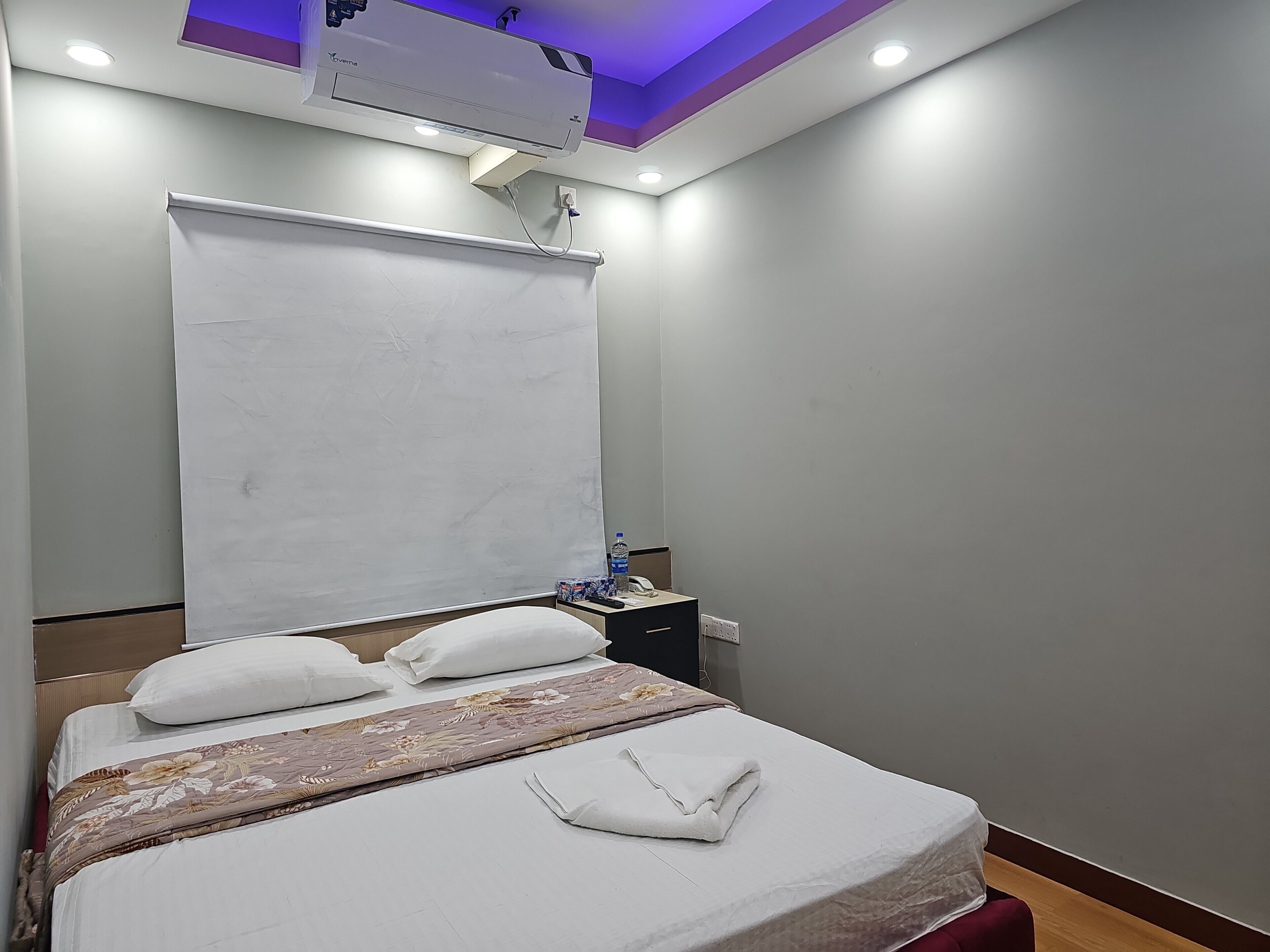 A hotel room with a bed, a bedside table with a water bottle, a phone, and a power outlet.