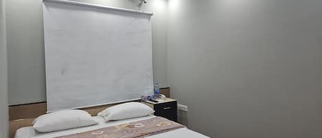 A hotel room with a bed, a bedside table with a water bottle, a phone, and a power outlet.