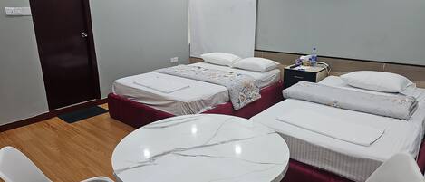 A hotel room with two single beds, a round marble table, two white chairs, a nightstand, and a door.