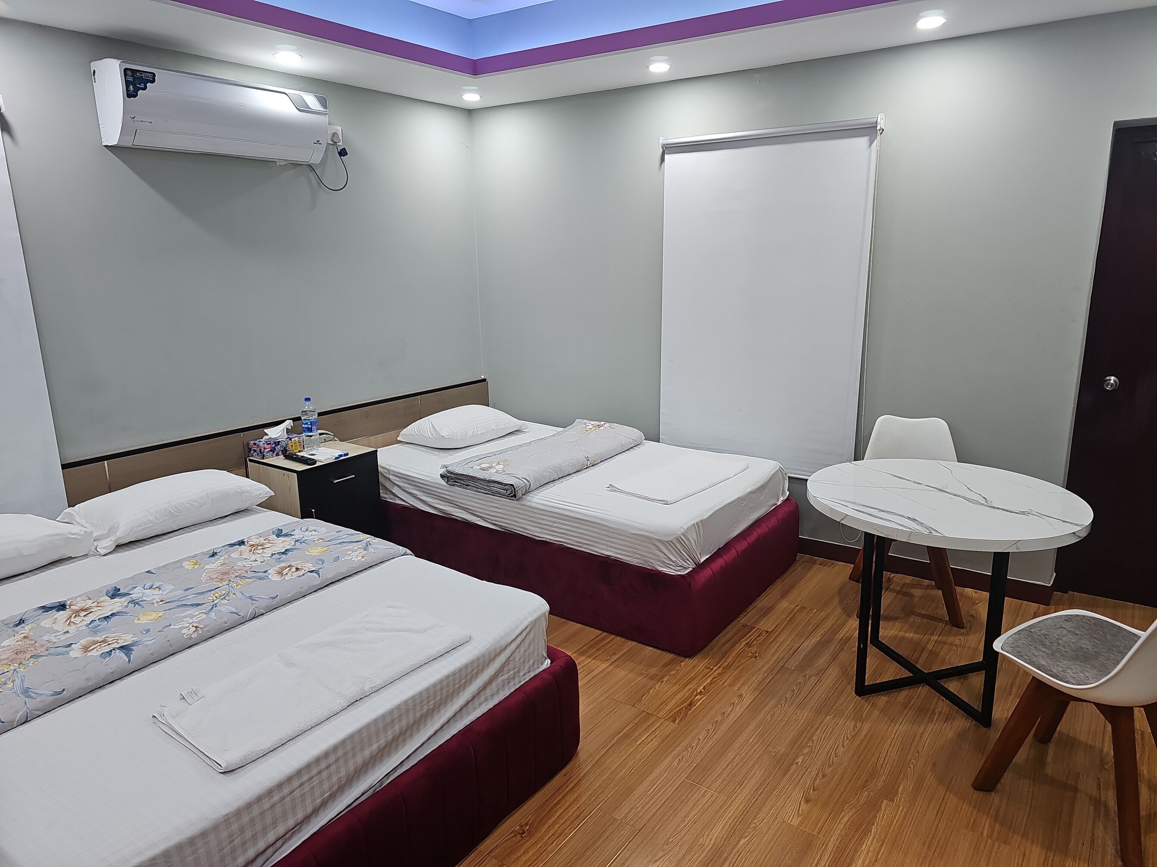 Habitación de hotel con dos camas, una mesita con una silla, un equipo de aire acondicionado y una ventana con persiana.