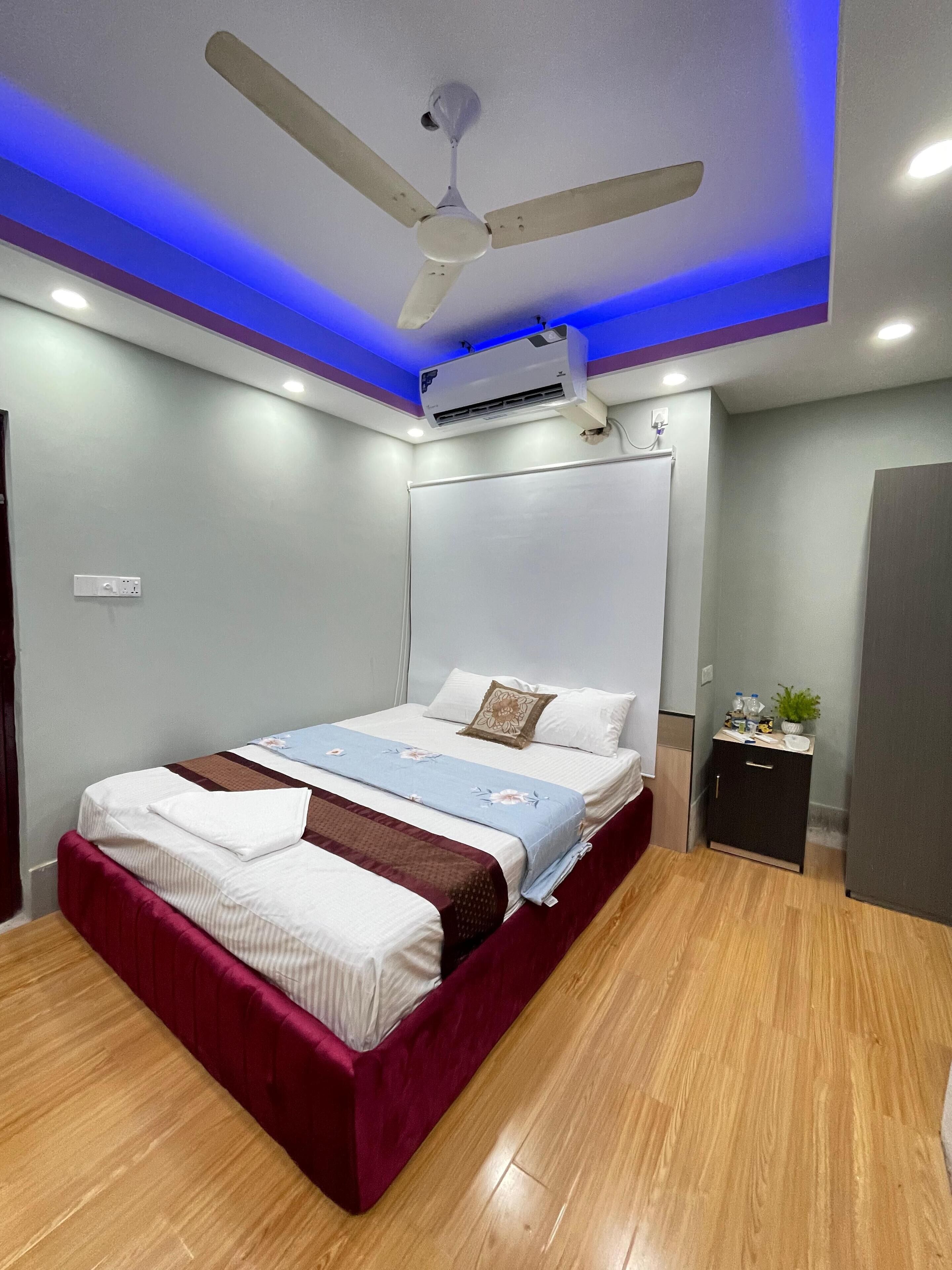 A modern bedroom with a bed, a ceiling fan, an air conditioning unit, and a small cabinet.