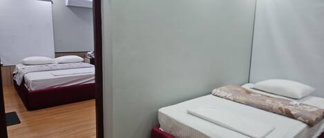 Habitación de hotel con dos camas, suelo de madera y pared blanca.