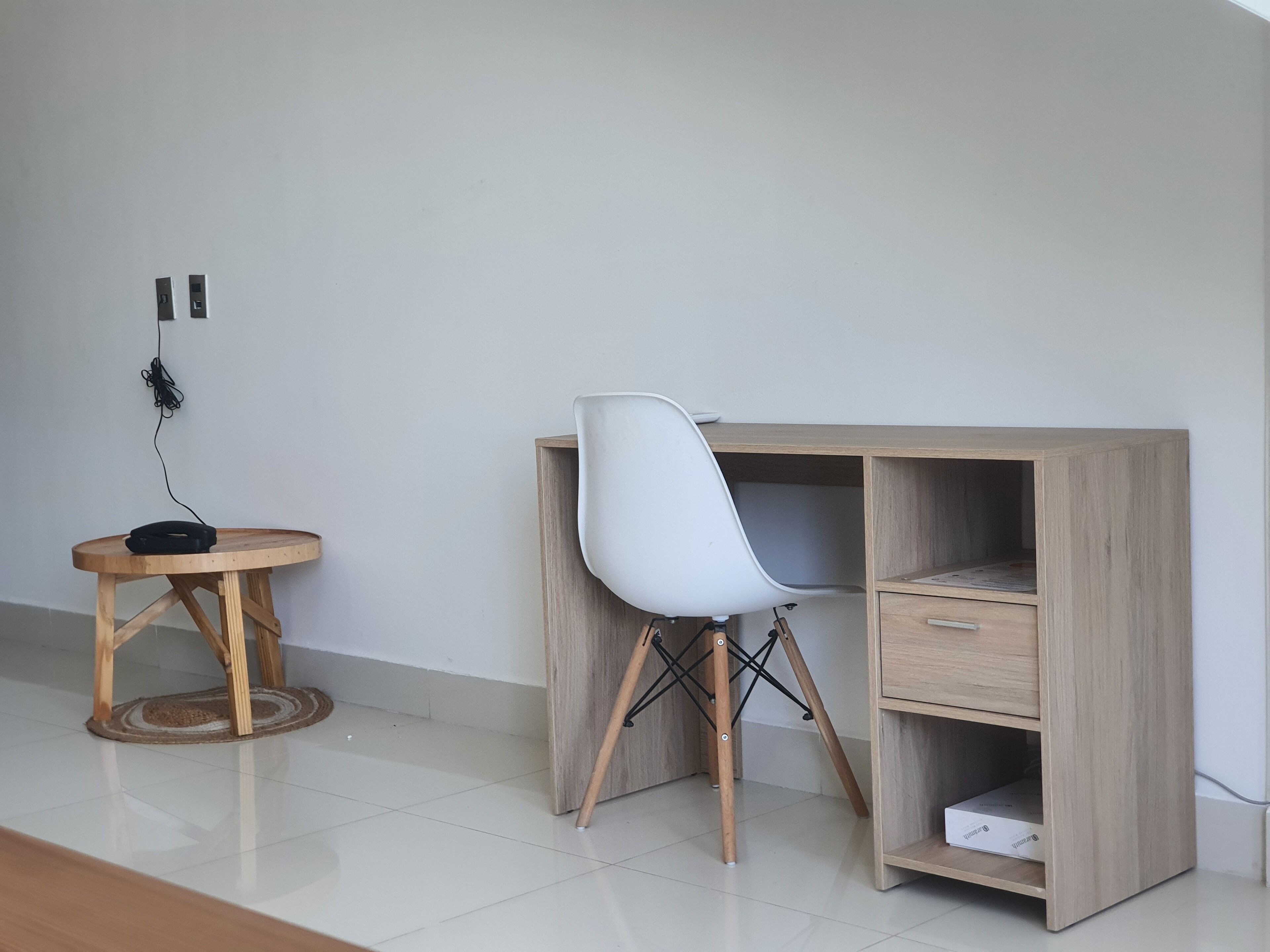 A modern, minimalist room with a wooden desk, a white chair, and a small round table with a coiled cable.