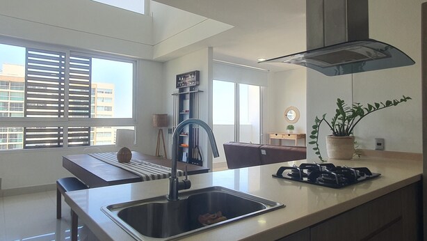 A modern kitchen with a stainless steel sink, a built-in stove, and a large window providing natural light. - Penthouse de lujo (Barranquilla)