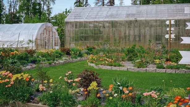 Invernadero con techo transparente, rodeado de diversas plantas con flores y un jardín bien cuidado.