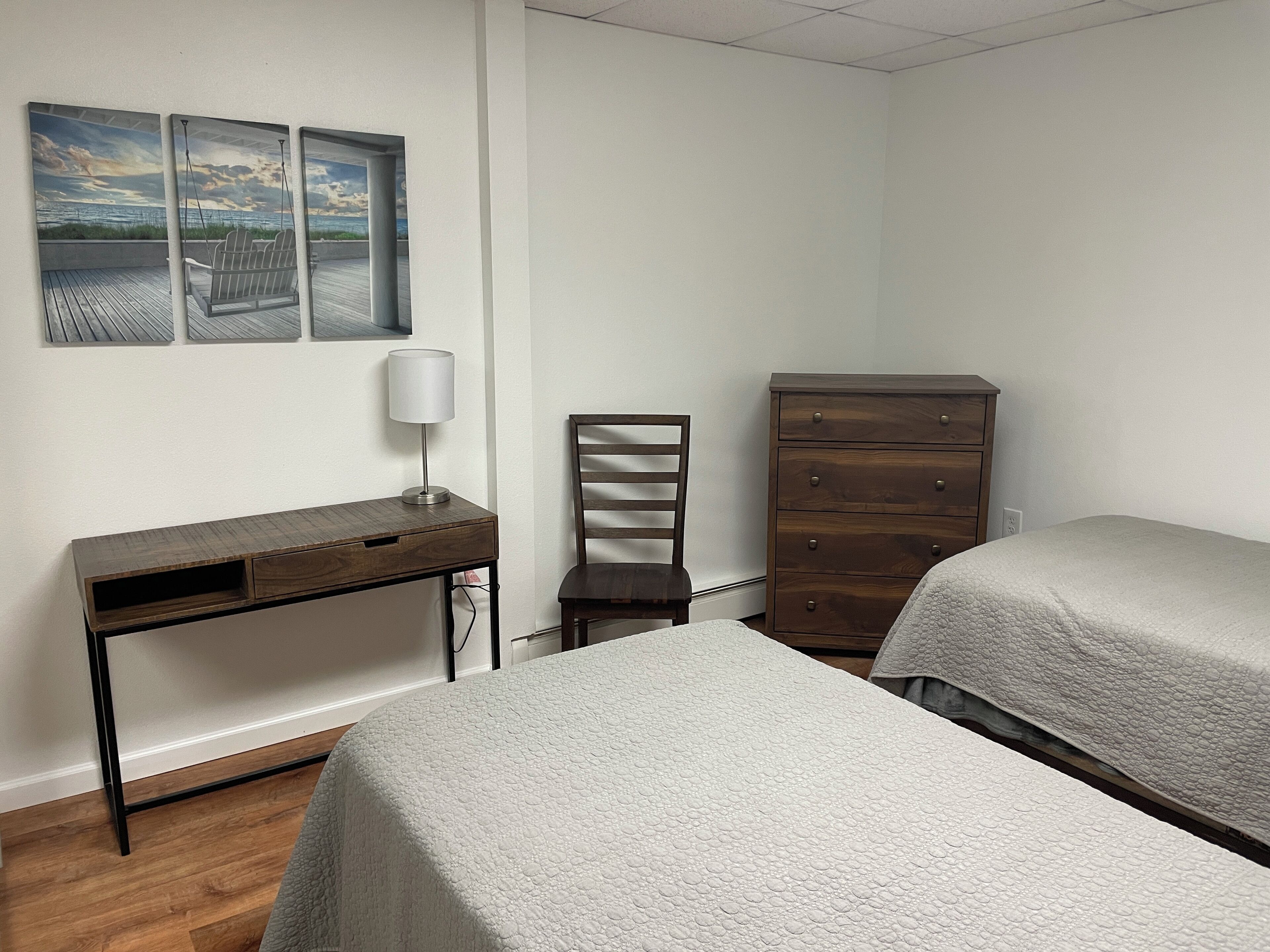 Une chambre avec deux lits, un bureau, une chaise, une commode et trois œuvres d’art murales.