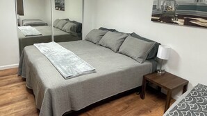 Un dormitorio con una cama, una mesita de noche con lámpara, un espejo y un cuadro en la pared.