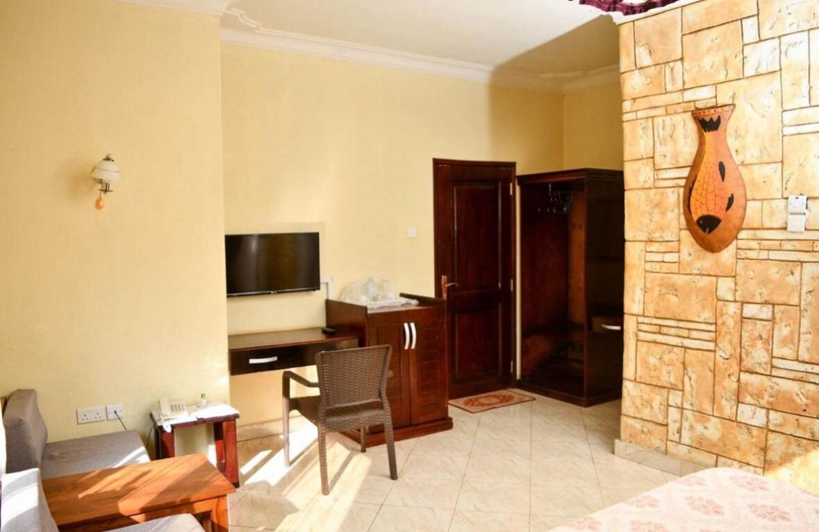 A room with a TV, wooden wardrobe, and a decorative wall piece.