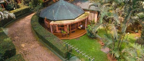 A circular building with a conical roof, surrounded by a well-maintained garden with palm trees and a paved walkway.