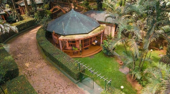 A circular building with a conical roof, surrounded by a well-maintained garden with palm trees and a paved walkway.
