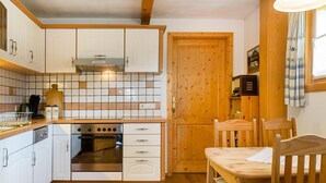Cocina compacta con armarios blancos, horno empotrado y una mesa de madera con sillas.