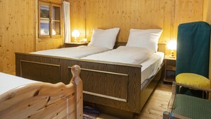 Una habitación de madera con una cama, una silla y una mesita de noche con una lámpara.
