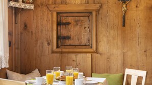 Una mesa de comedor de madera con alimentos para el desayuno, como jugo de naranja y pasteles, frente a una pared de madera con una cruz.