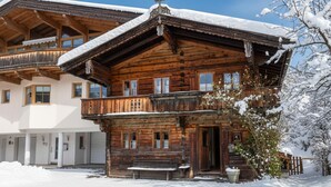 Una cabaña de madera con balcón, banco y jardín cubierto de nieve.