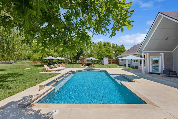 A rectangular swimming pool with a surrounding deck, lounge chairs, and umbrellas.