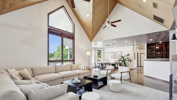 A spacious living area with a high ceiling, a large window, and a modern kitchen in the background. - The Perfect Getaway 5BR/4BA with Pool & Hot Tub (Ponder)