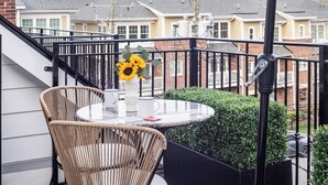 A balcony with a round table and two wicker chairs, a white umbrella, and a potted plant. - Stylish 2BR Condo in Newly Restored Church (Charlotte)