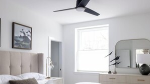 A bedroom with a bed, a ceiling fan, a window, a dresser, and two framed pictures on the wall. - Stylish 2BR Condo in Newly Restored Church (Charlotte)