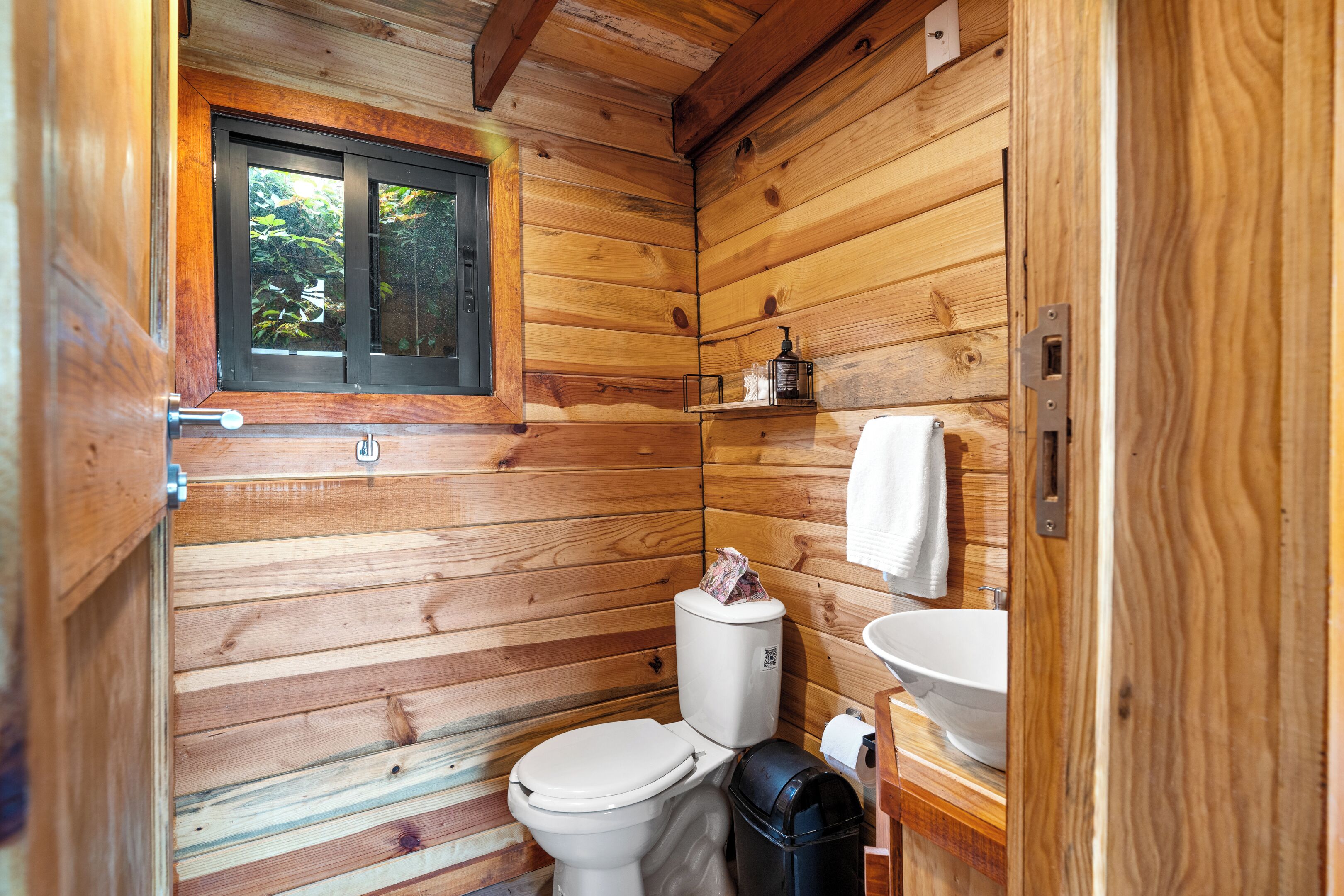 A wooden cabin bathroom with a toilet, sink, and window.