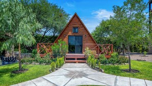 Una cabaña de madera con techo triangular, una puerta principal y un ventanal pequeño.