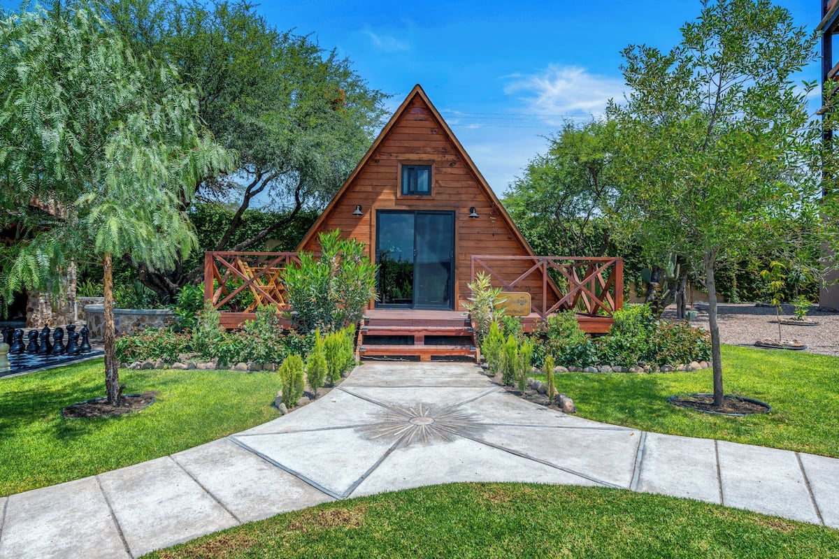 Una cabaña de madera con techo triangular, una puerta principal y un ventanal pequeño.