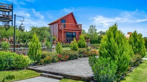 Una casa de madera roja con balcón, rodeada de jardines cuidados y un camino empedrado.