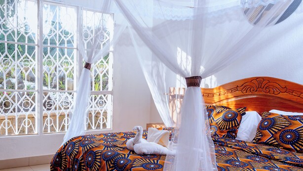 Una cama con dosel, ropa de cama estampada y una vista a través de una ventana con celosías metálicas decorativas.