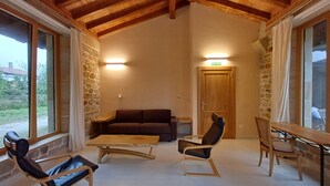 A cozy room with a stone wall, wooden ceiling beams, a sofa, two rocking chairs, a table, and a door marked "SALIDA".