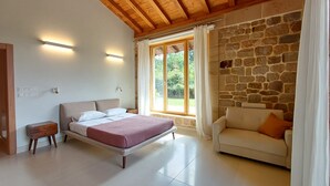 A bedroom with a bed, a nightstand, a stone wall, a window with curtains, and a wooden ceiling.