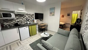 Un espacio habitable compacto con kitchenette, un sofá, una mesita y un televisor.