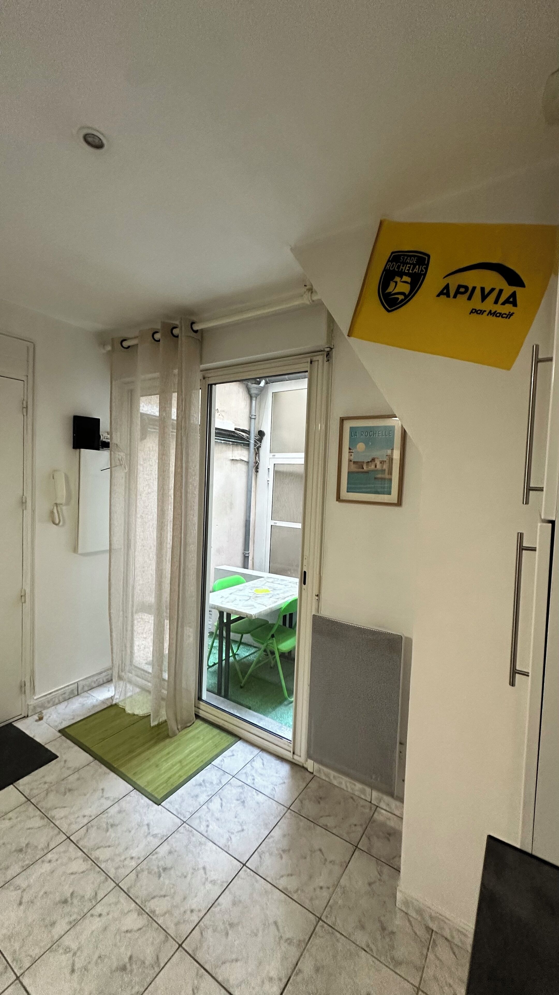 Une chambre d’hôtel dotée d’une porte-fenêtre coulissante donnant sur un balcon, d’un tableau encadré accroché au mur et d’une pancarte jaune au-dessus de la porte.