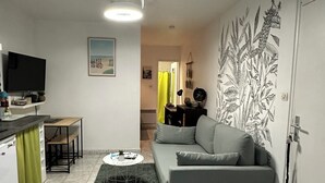 Un espacio habitable compacto con sofá, una pequeña mesa de comedor, televisor y cocina equipada con refrigerador y microondas.