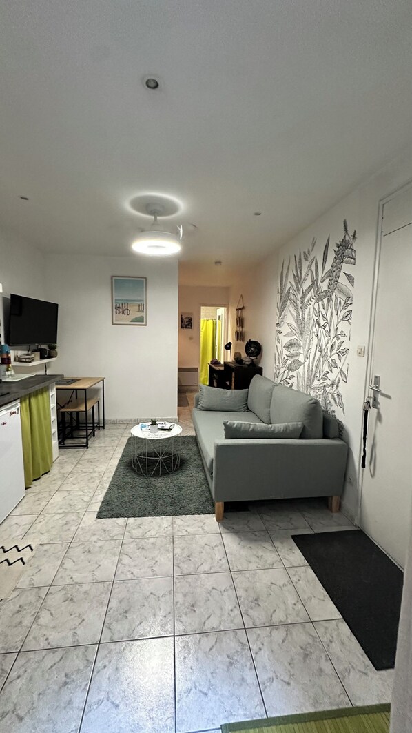 A compact living space with a sofa, a small dining table, a TV, and a kitchen area with a refrigerator and a microwave. - Appartement Situé Directement sur le Vieux Port de La Rochelle (La Rochelle)