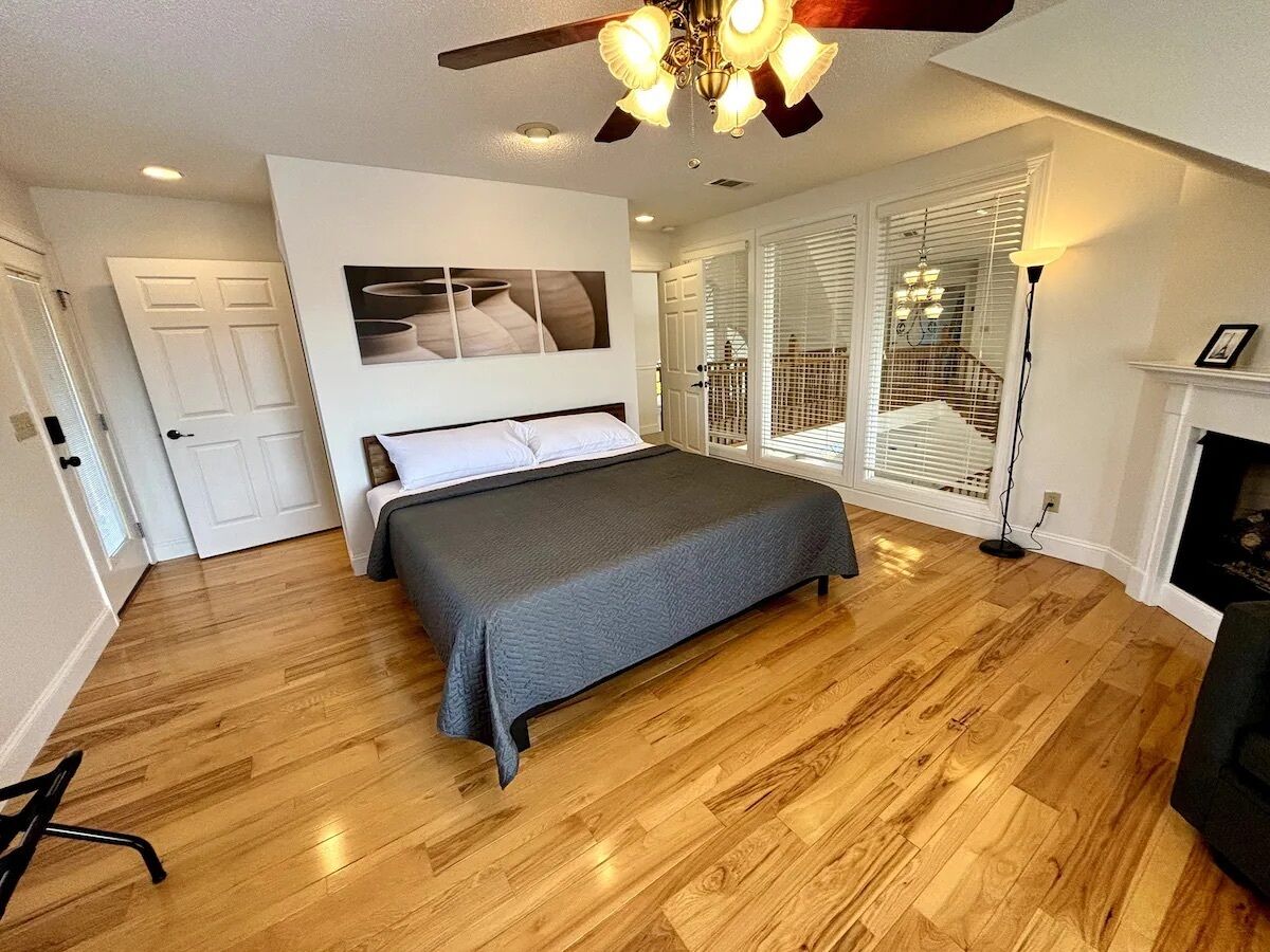 A bedroom with a bed, a ceiling fan, a fireplace, and a door.