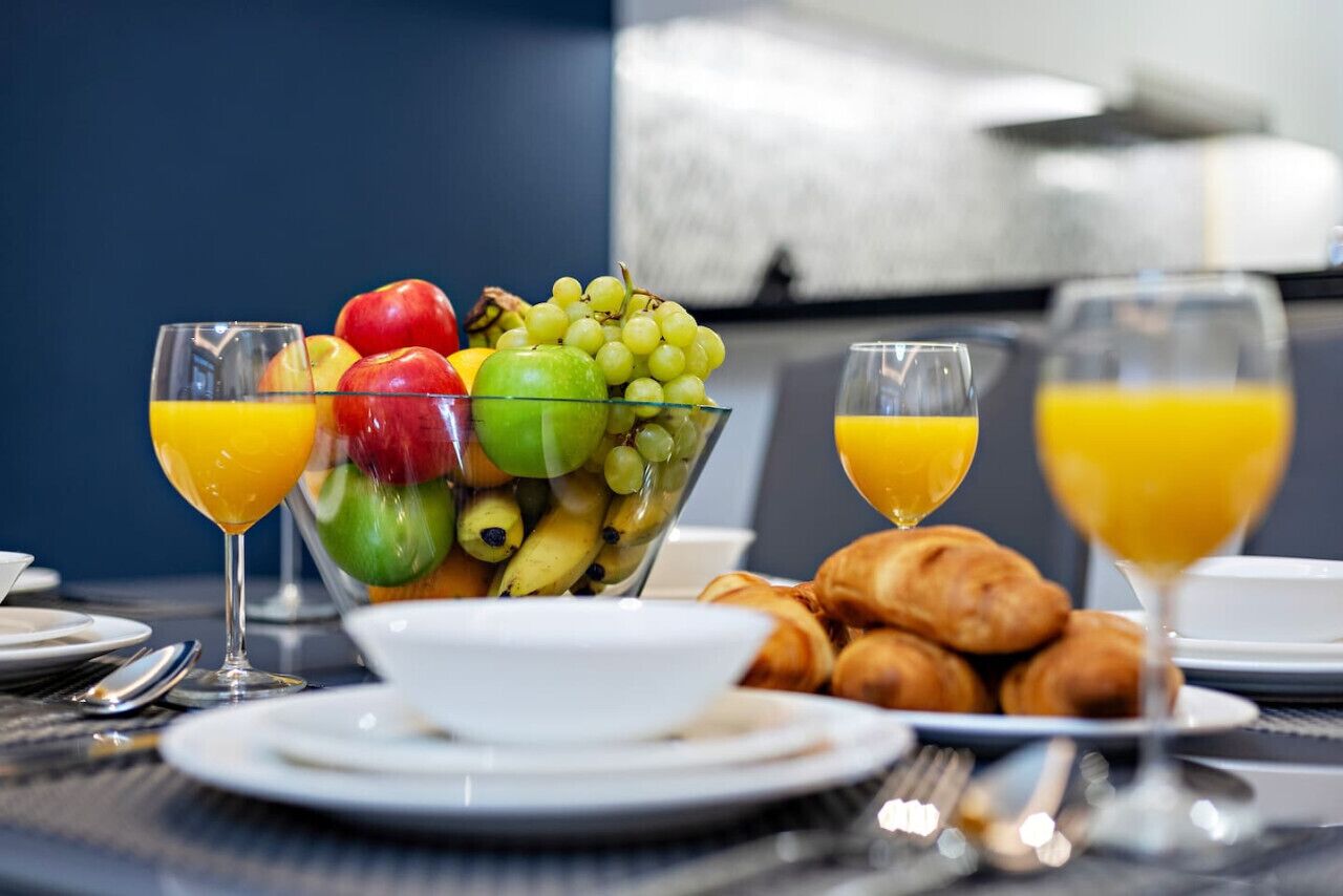 A breakfast setting with a fruit bowl, croissants, and glasses of orange juice.
