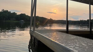 A wooden dock extending over calm water, with a sunset in the background and a forested shoreline.