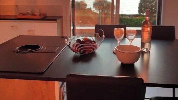 Een eetgedeelte met uitzicht op zee, een tafel met een schaal fruit, een wijnglas en een fles.