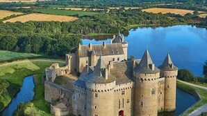 Een kasteel met meerdere torens, omringd door water en groen.