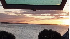 Uitzicht vanuit een raam op een waterpartij bij zonsondergang.