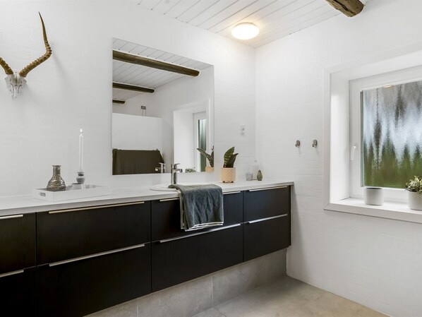A modern bathroom with a white vanity, dark cabinets, a large mirror, and a window with a view of trees.