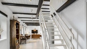 A spacious hallway with a white staircase leading to an upper floor. A wooden cabinet and a television are visible in the room. - "Thorgot" - 3km from the sea by Interhome (Pandrup)