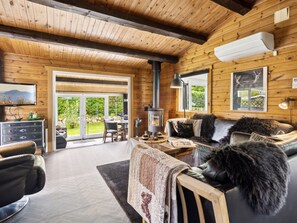 A cozy cabin interior with a fireplace, leather furniture, and a large window overlooking a garden.