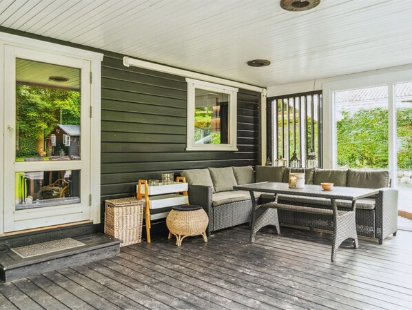A covered porch with a dark green exterior, wicker furniture, and a table with a bowl.