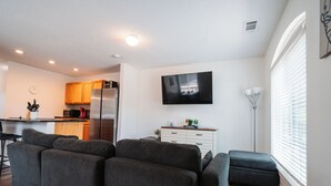 Een moderne woonkamer met een zithoek, een flatscreen televisie en een keuken op de achtergrond.