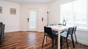 Een kamer met een witte deur, een eettafel met stoelen, een lamp en kunst aan de muur.